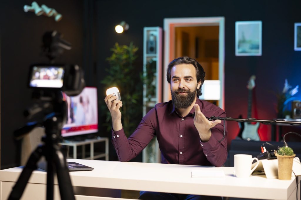 Influencer in dimly lit apartment studio filming smart light bulb review for online streaming platforms with professional camera. Internet star films IoT home automation product with specialized gear.
