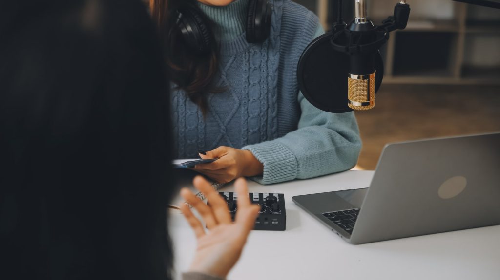 Woman recording a podcast on her laptop computer with headphones and a microscope. Female podcaster making audio podcast from her home studio.