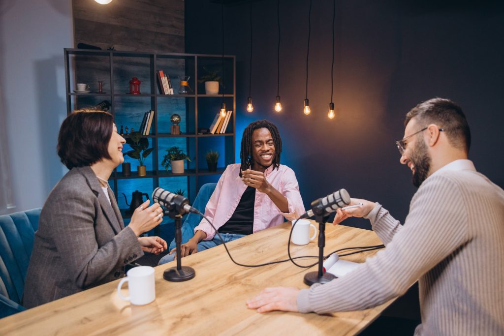 Podcast hosts collaborating in soundproof studio, microphones capturing energetic discussion and shared laughter between creative professionals.