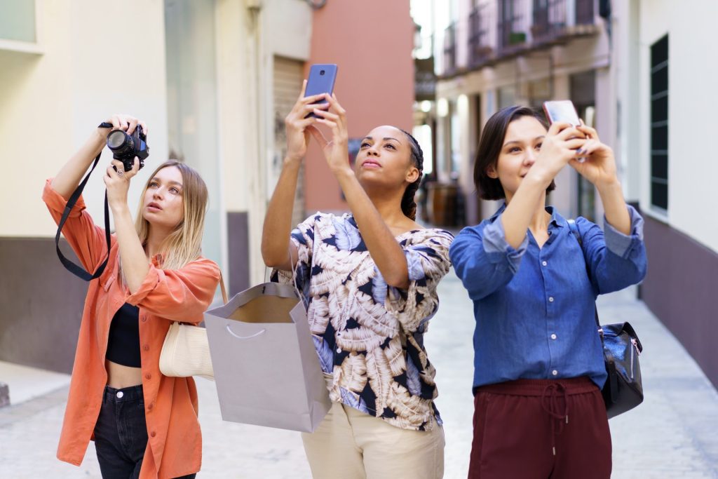 Stylish young diverse women taking photos during vacation in old city.