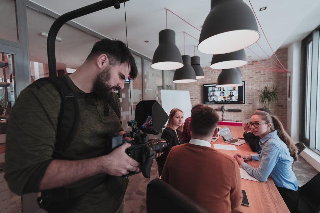 Behind the scene. Cameraman recording a group of young multiethnic business people working and communicating together in a creative office. Selective focus. High-quality photo.